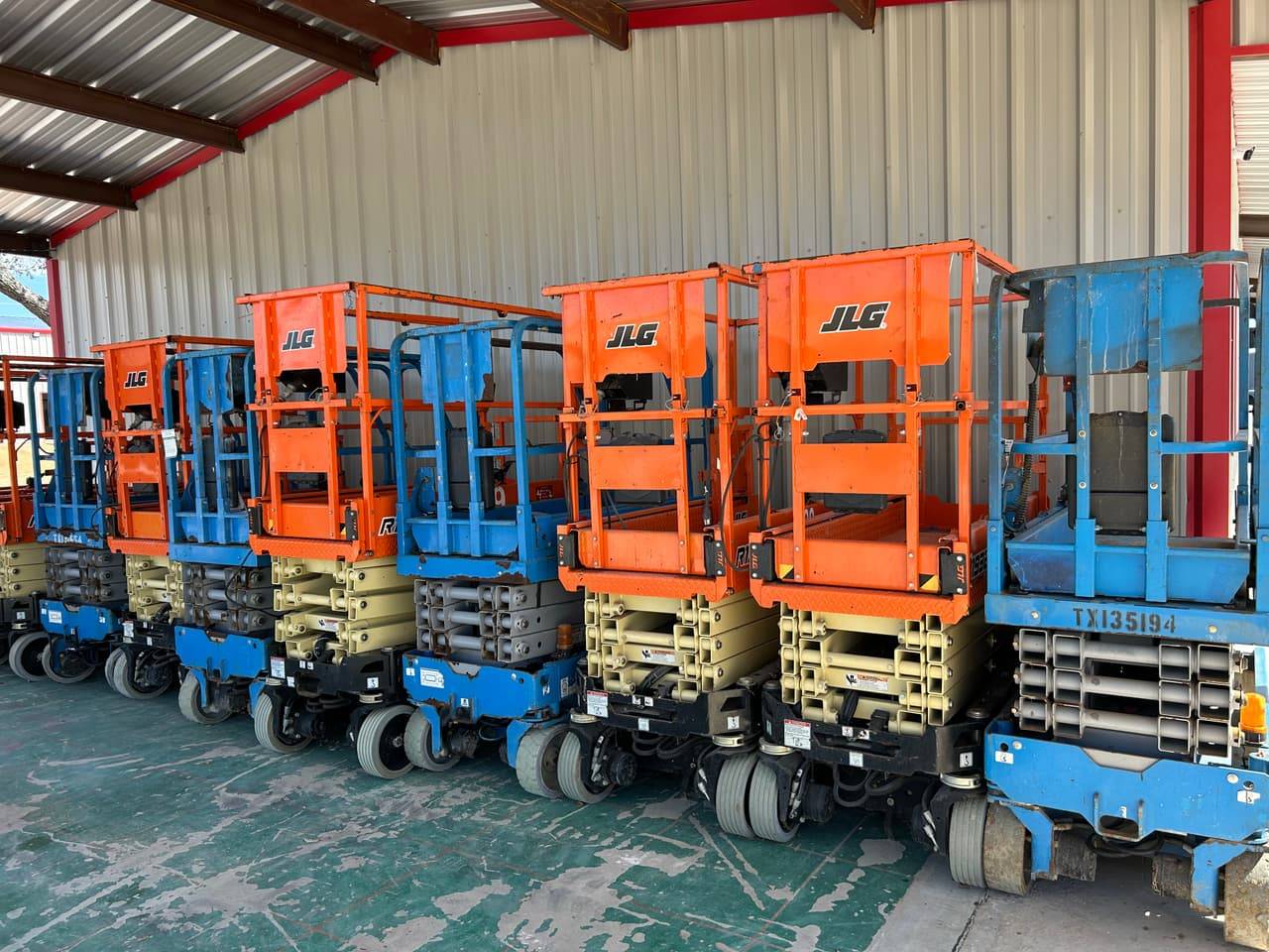 Row of JLG and Genie electric scissor lifts parked under cover at 4-T Rental & Sales